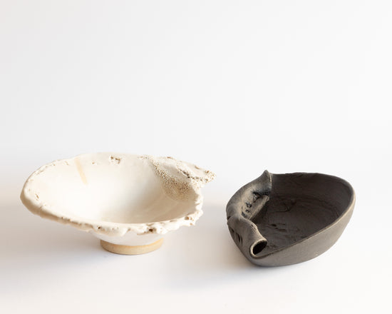 Two wheel-thrown ceramic bowl, one black and one white, with a deformed shape