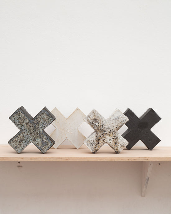 Four ceramic cross-shaped objects in a row, glazed in black, white, and a hint of blue