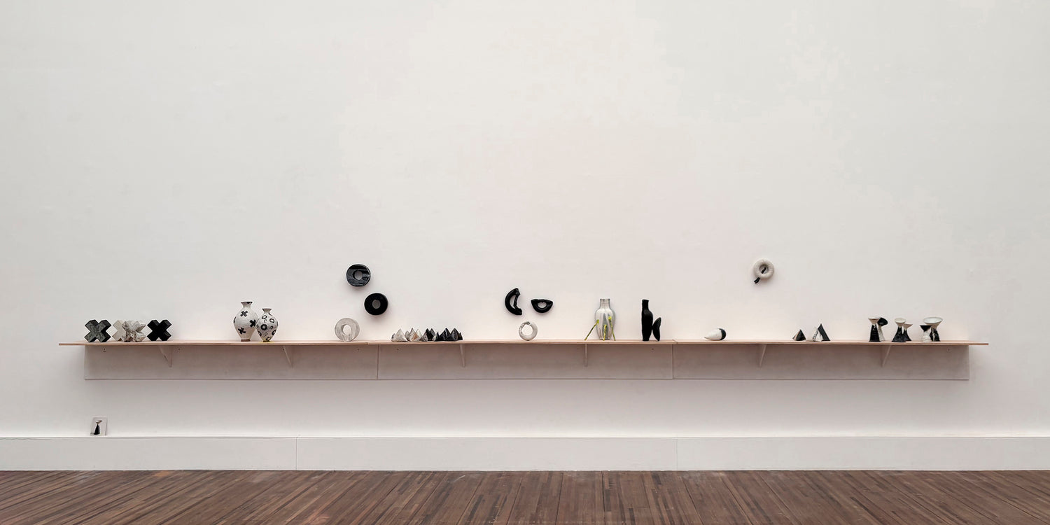 Long shelf displaying groups of black and white ceramic objects at Kunsthal Mechelen