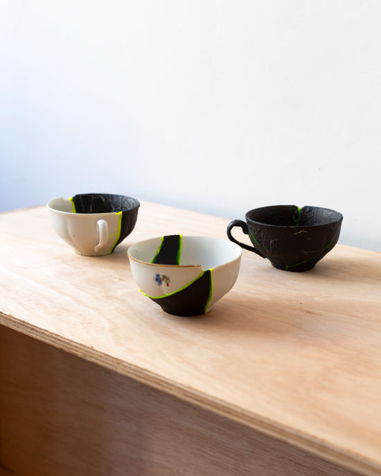 Three thrifted porcelain cups, broken and reassembled with fluorescent yellow adhesive