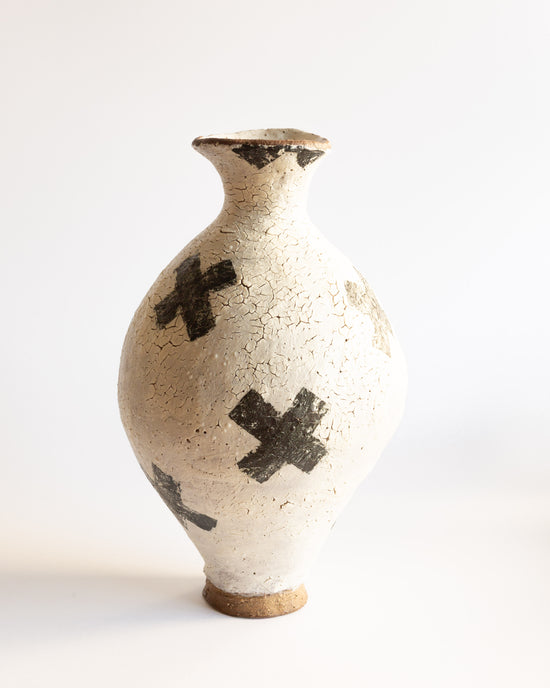 White coil-built ceramic vessel with black crosses and a cracked surface